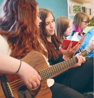 Kuva: Kirkon kuvapankki, kuvaaja Suvi Pietilä. Rippikoulussa lauletaan, yksi nuorista soittaa kitaraa.
